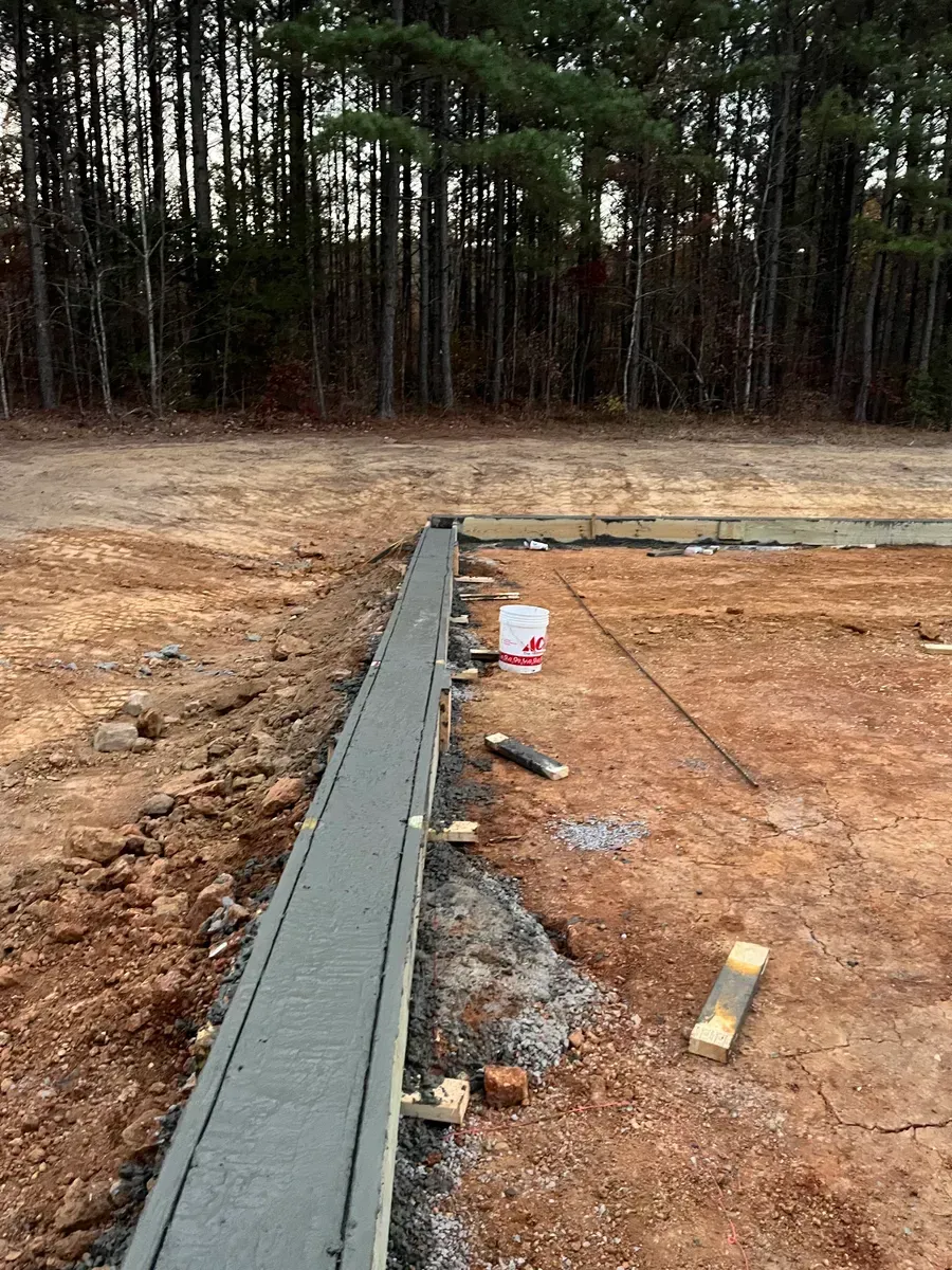 A concrete wall is being built in a dirt field with trees in the background.