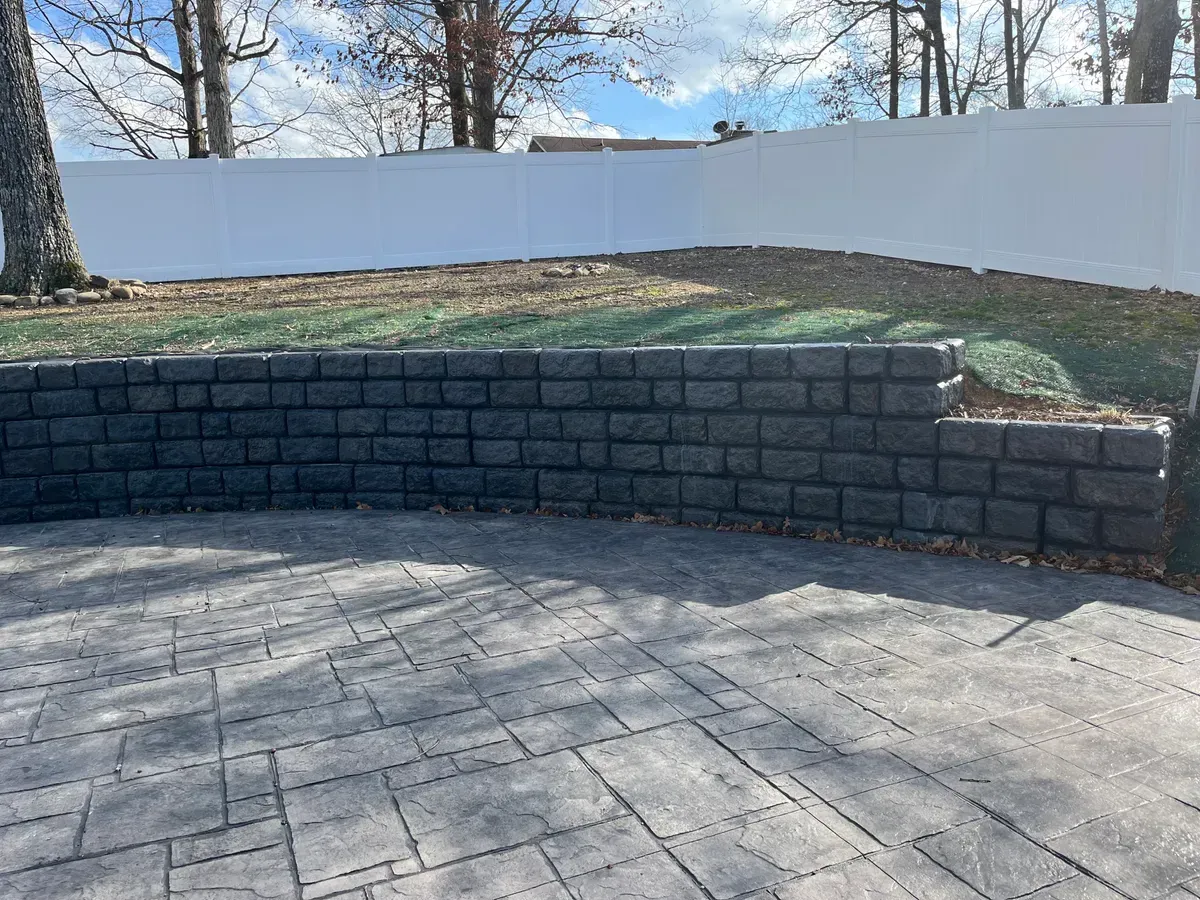 A brick wall surrounds a patio with a white fence in the background.