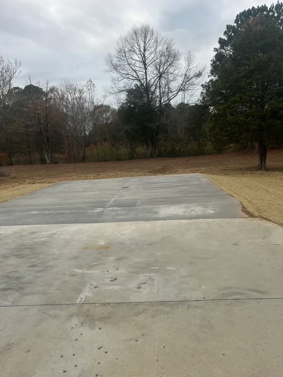 A concrete driveway with trees in the background and a cloudy sky.