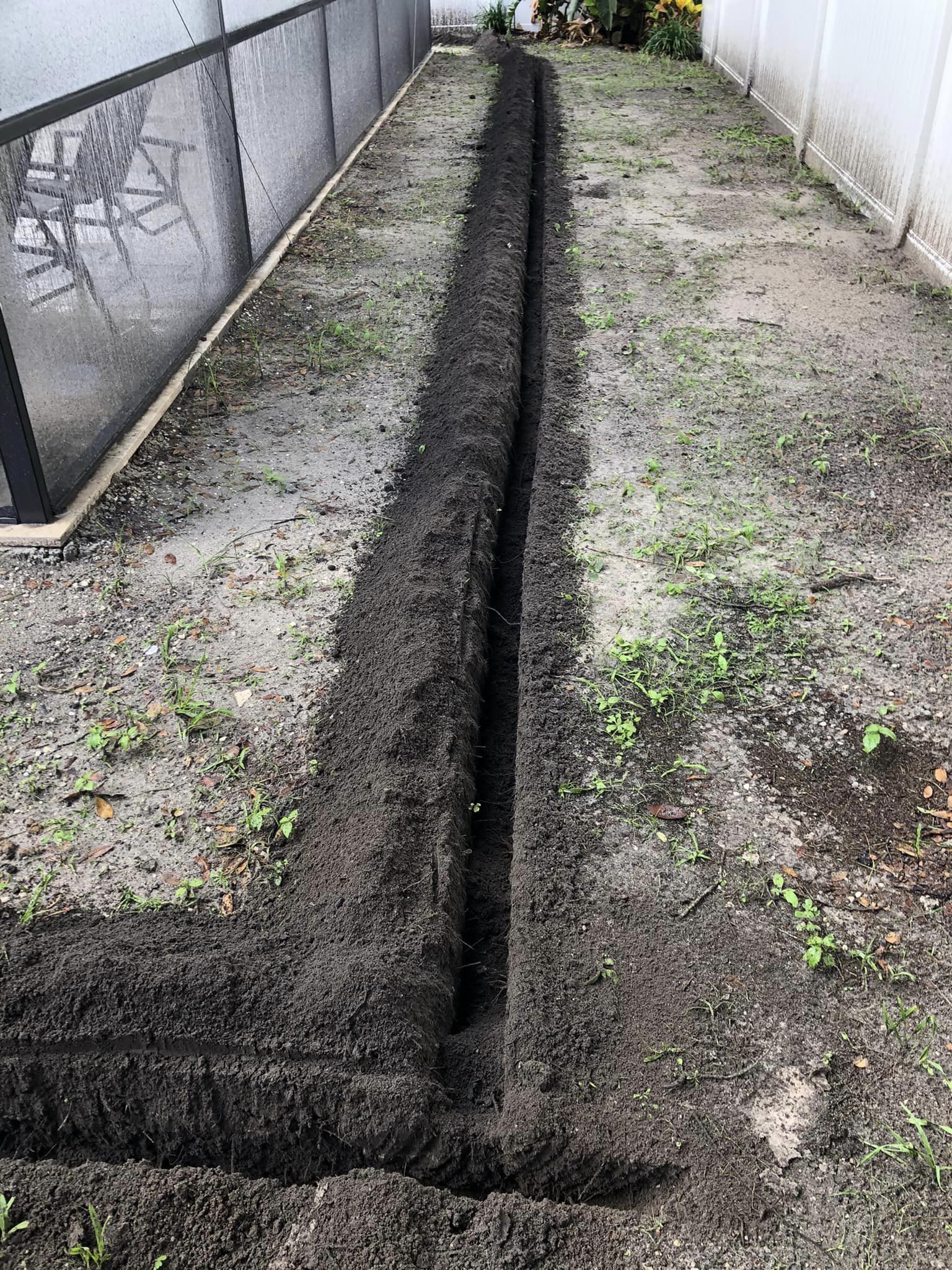 A long trench is being dug in the dirt in a backyard.