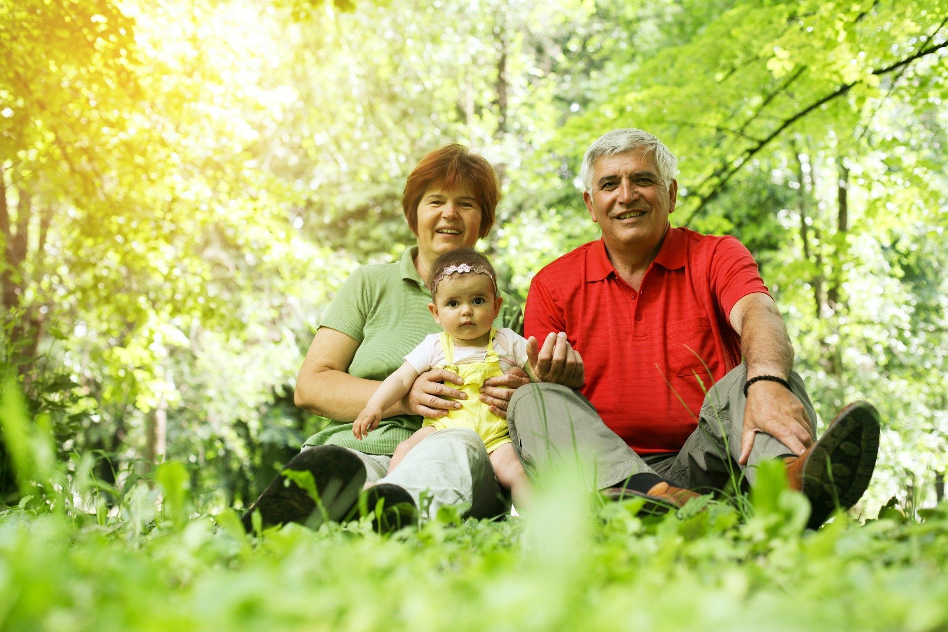 Grandparents with a baby in a sunny park, smiling.