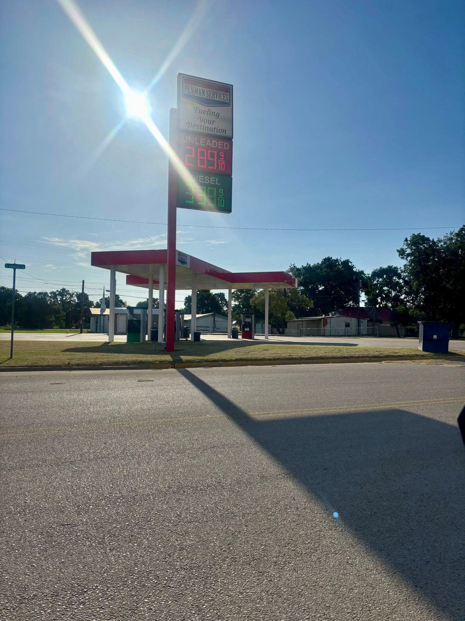 Gas station with red and white canopy under bright sunlight and blue sky.