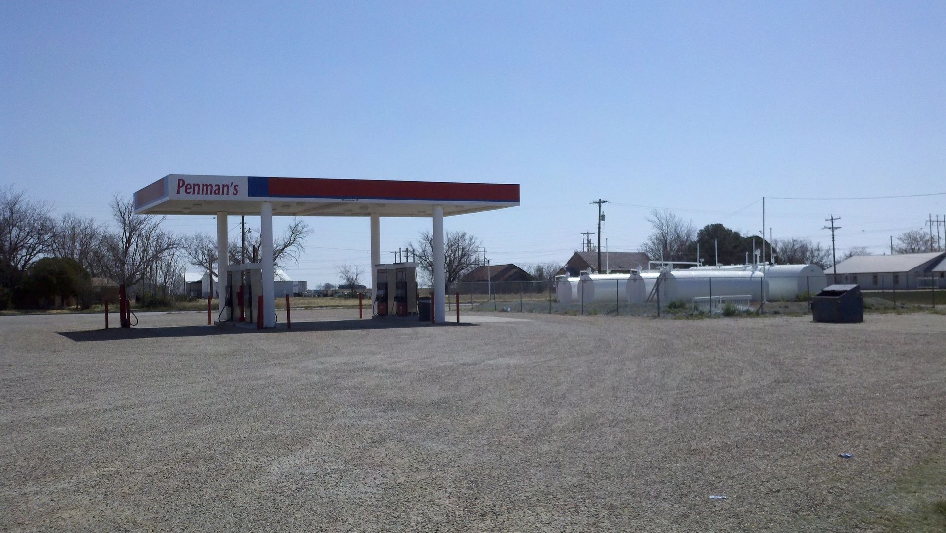 Gas station with a red and blue canopy; gravel lot; clear sky.