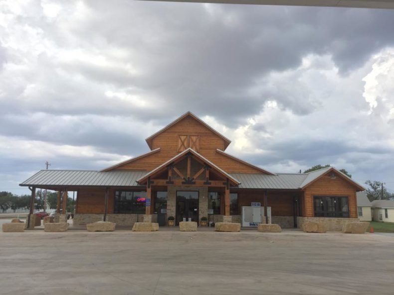 Rustic-style restaurant with brown wooden exterior, gray metal roof, and stone accents. Cloudy sky above.