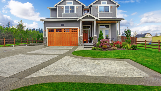 Backyard patio with gravel surface, grill, table, and umbrella. House siding and retaining wall with landscaping.