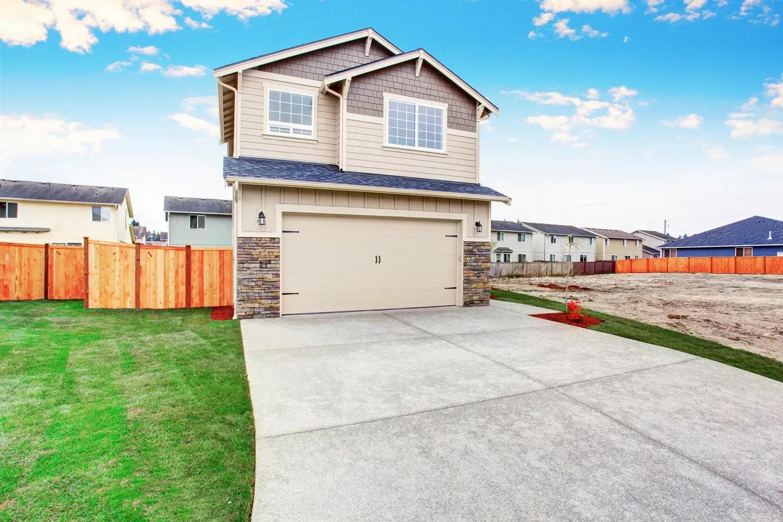 Two-story beige house with garage and concrete driveway under a blue sky.