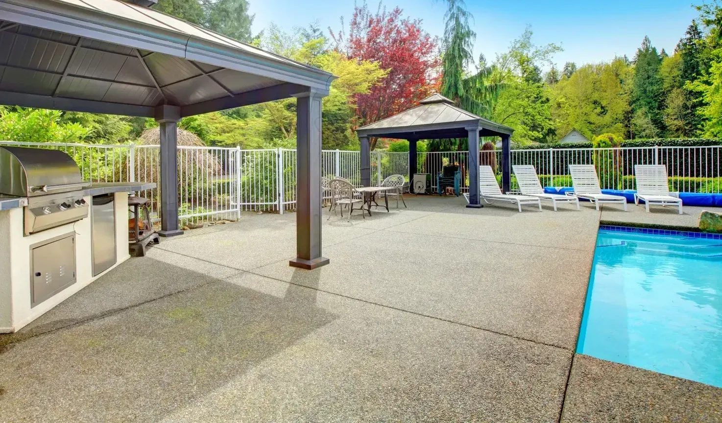 Outdoor patio with swimming pool, grill, gazebos, and lounge chairs; sunny day.