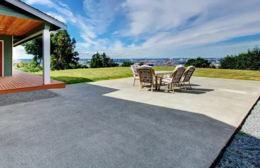 Patio with table, chairs, and house overlooking distant city under blue sky.