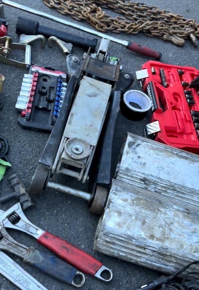 A bunch of tools are laying on the ground including a jack