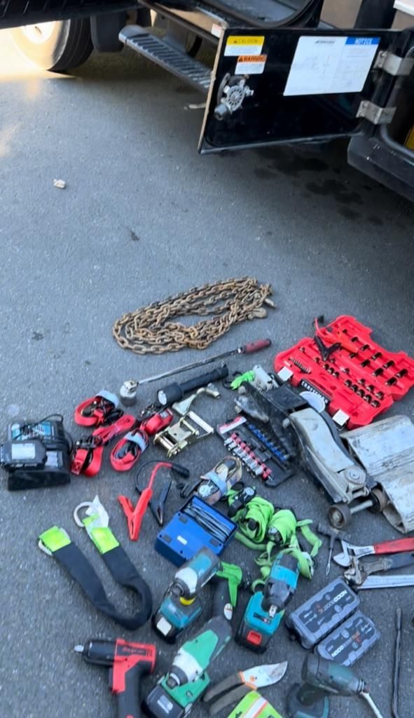 A bunch of tools are laying on the ground next to a car.