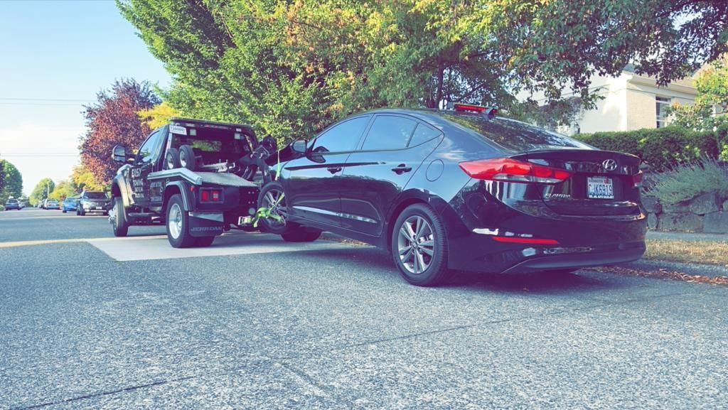 A black car is parked on the side of the road next to a tow truck.