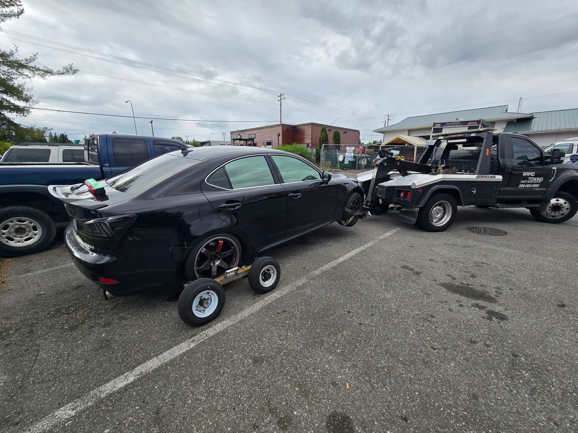 A tow truck is towing a white car on a highway.