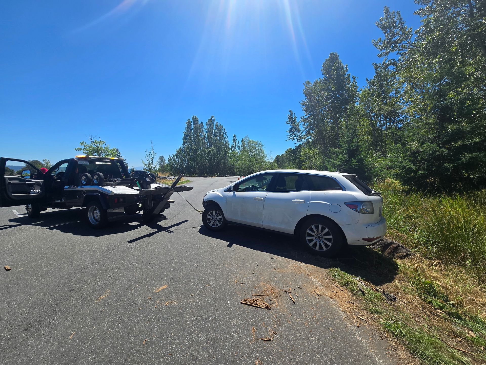 A white suv is sitting on the side of the road next to a tow truck.