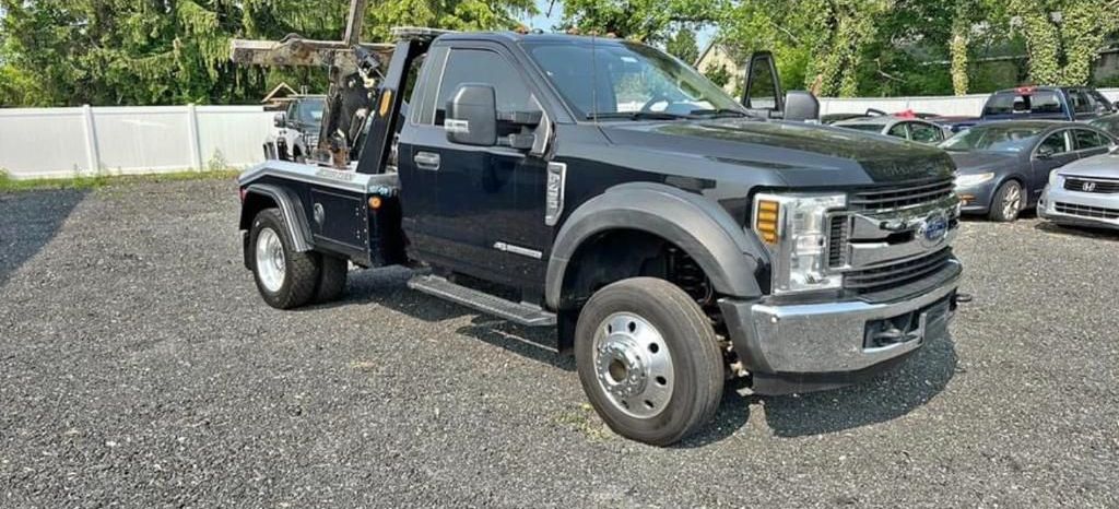 A black tow truck is parked in a gravel lot.
