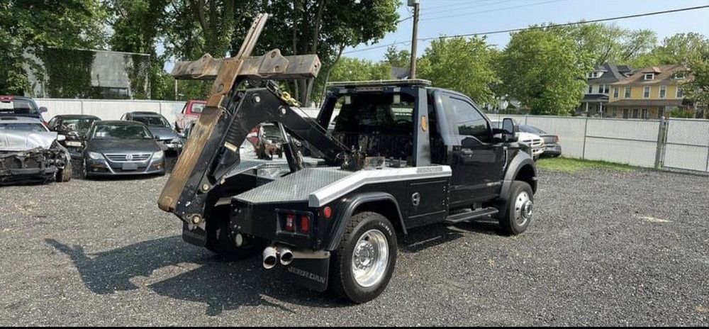 A black and silver tow truck is parked in a gravel lot.