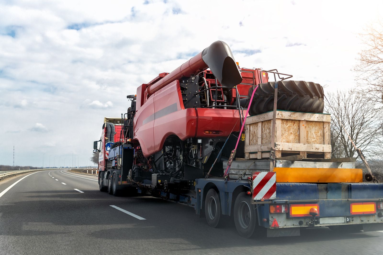 A semi truck is carrying a combine harvester down a highway.