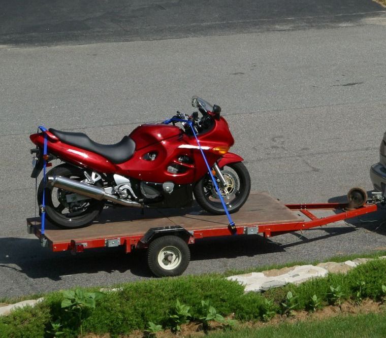 A silver car is towing a red motorcycle on a trailer
