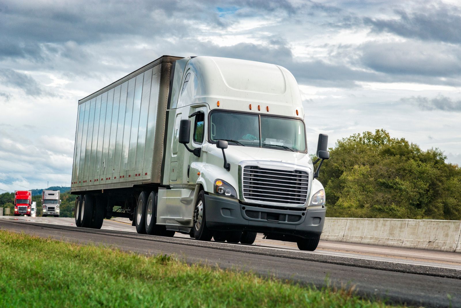 A semi truck is driving down a highway next to a grassy field.