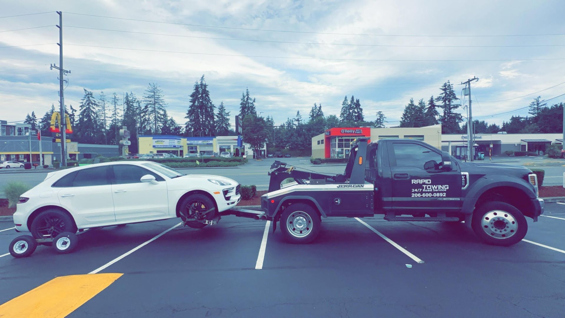 A tow truck is towing a white car in a parking lot.