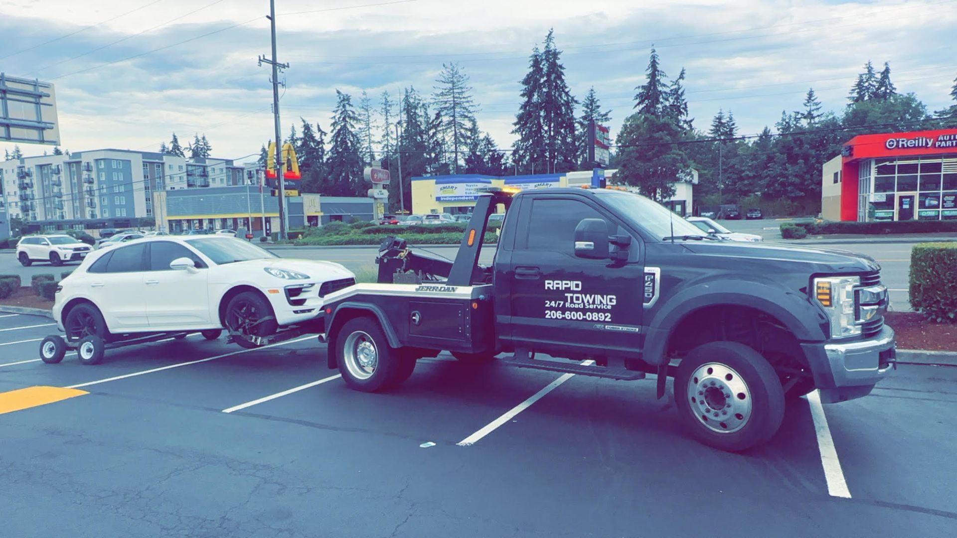 A tow truck is towing a white car in a parking lot.