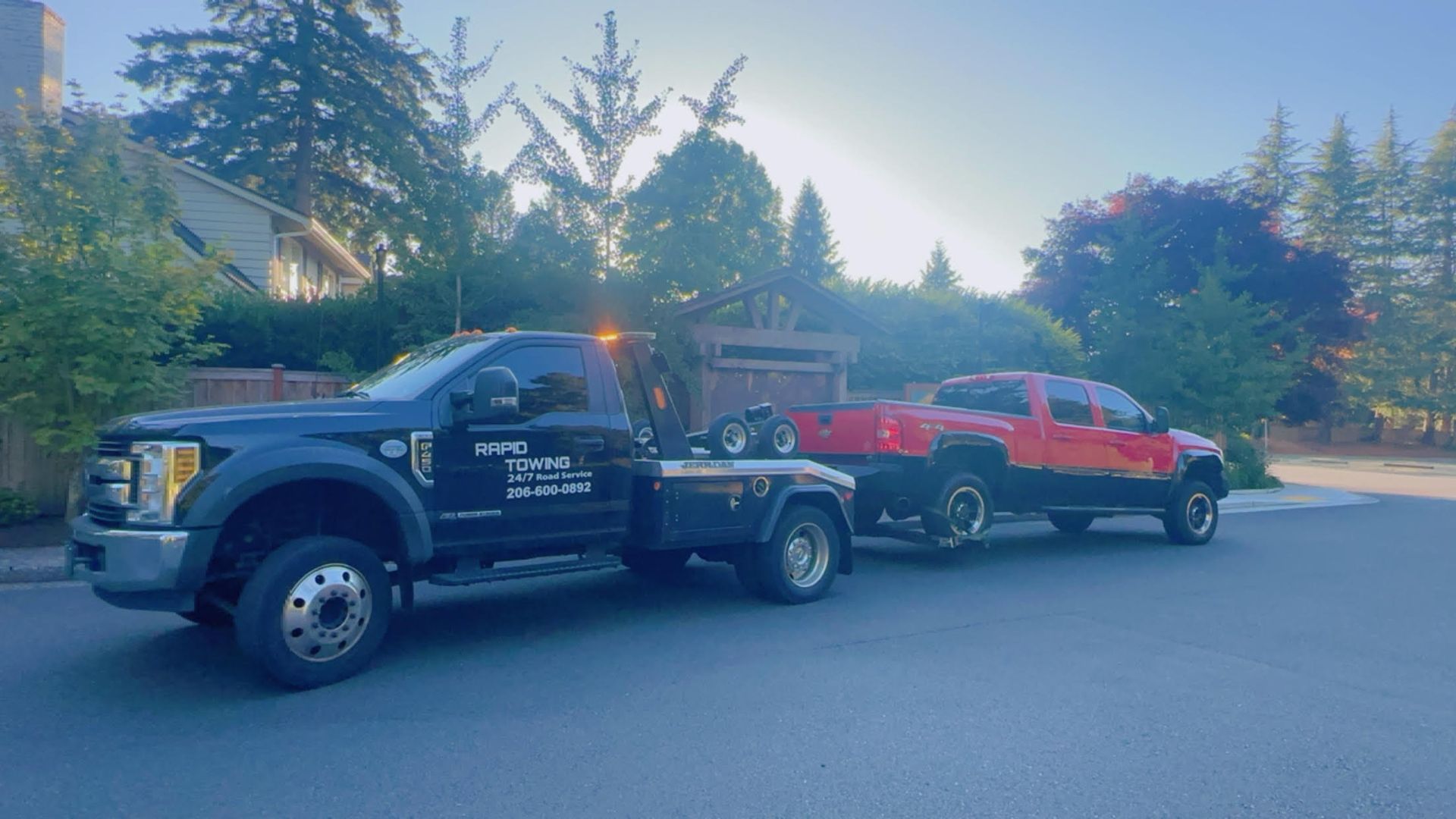A tow truck is towing a red truck down a street.