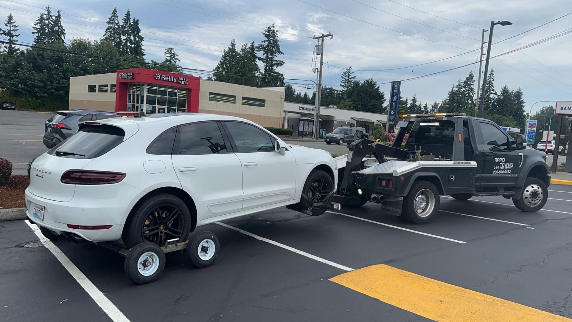 A white porsche macan is being towed by a tow truck in a parking lot.