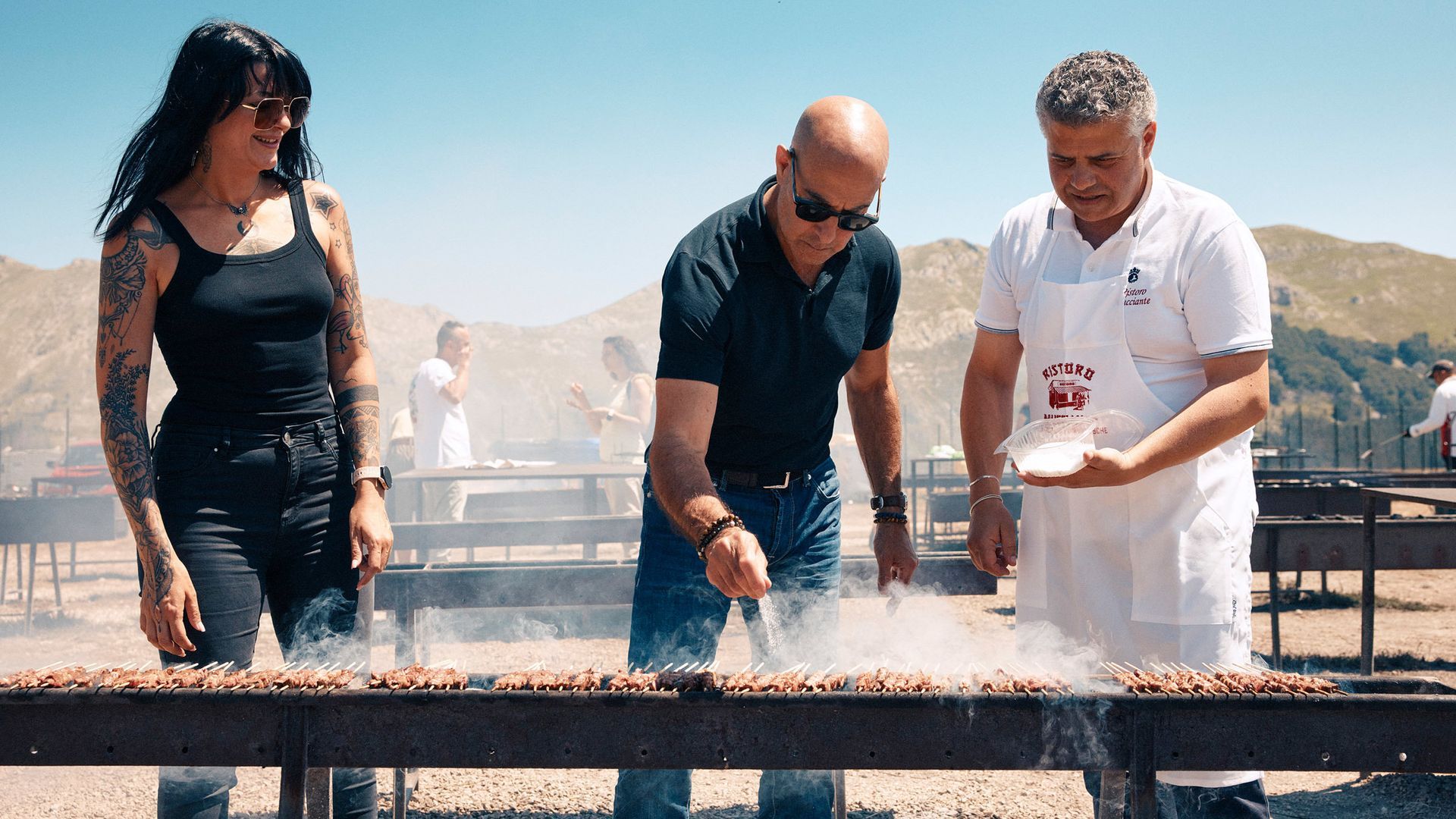 People grilling traditional Abruzzo arrosticini outdoors, surrounded by mountains—authentic Italian 