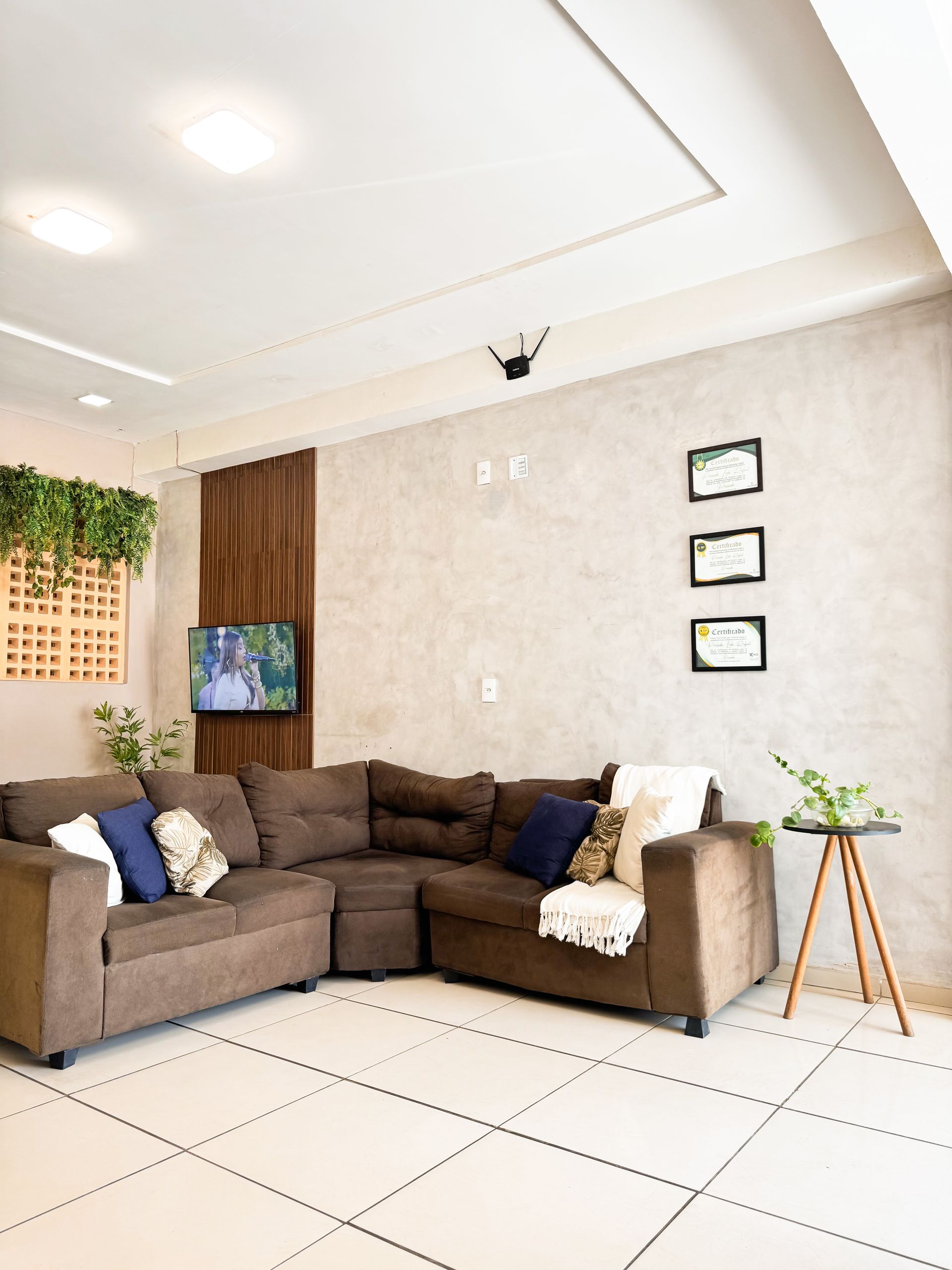 Sala de estar aconchegante com sofá modular marrom, TV, parede texturizada e plantas em vasos.
