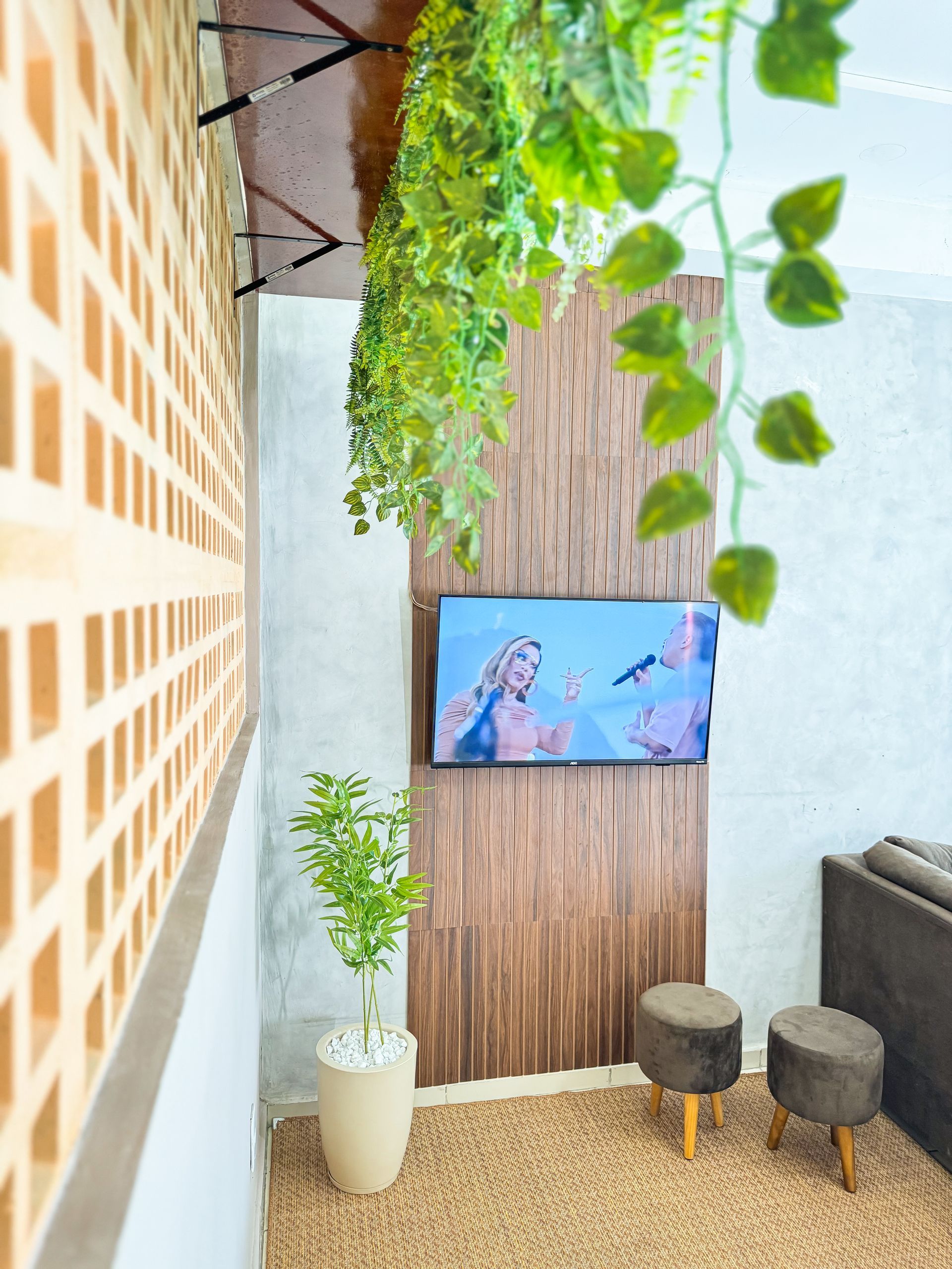 Sala com TV em parede texturizada, plantas, bancos e parede de tijolos.