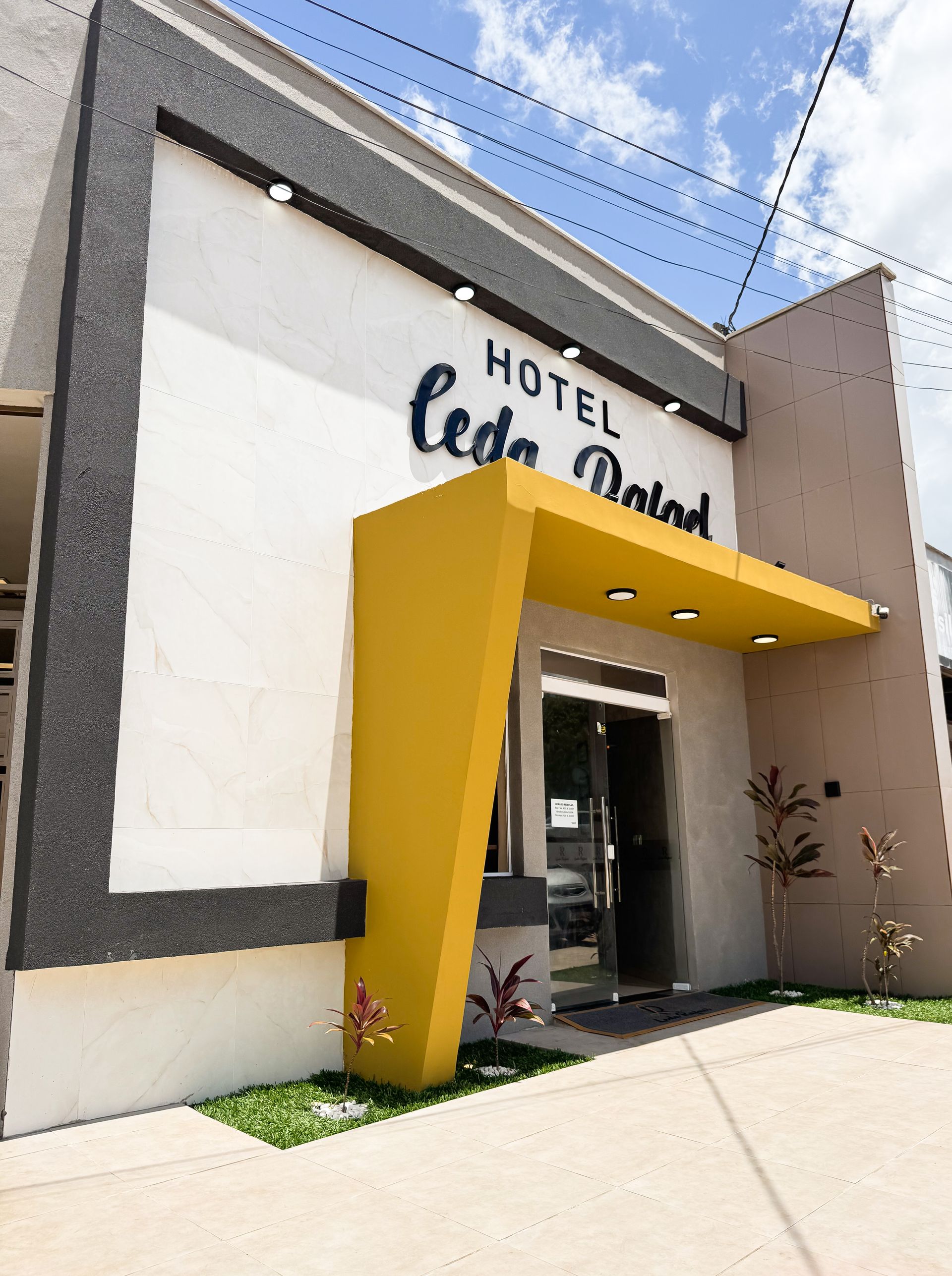 Entrada do Hotel Ceda Palad. Fachada amarela e cinza com portas de vidro abertas.
