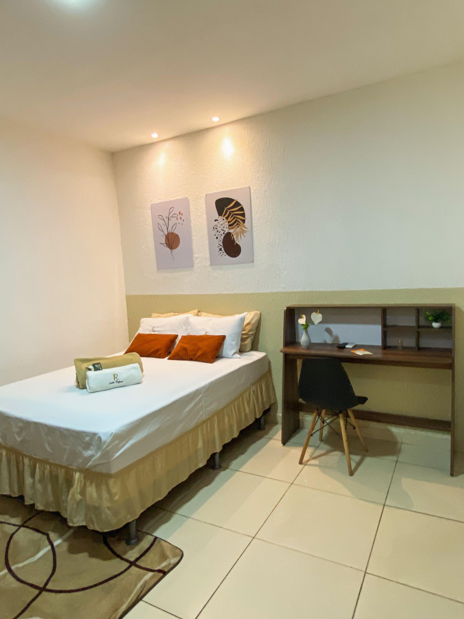 Quarto com cama, escrivaninha, obras de arte e tapete. Esquema de cores em tons de creme e dourado.