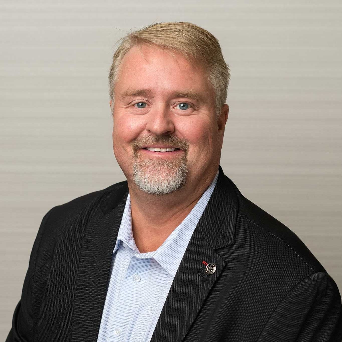 A man with a beard is wearing a suit and smiling for the camera.