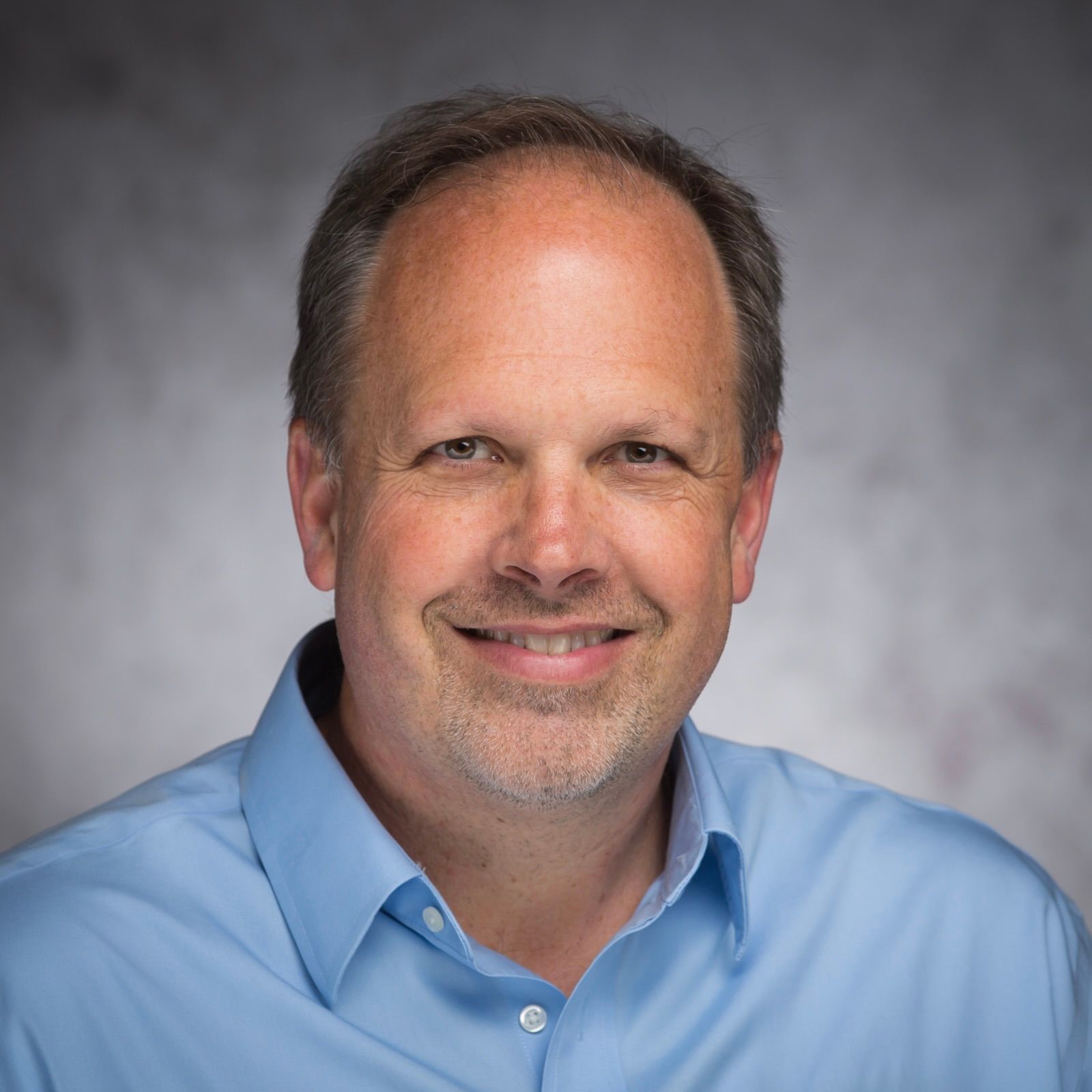 A man in a blue shirt is smiling for the camera.