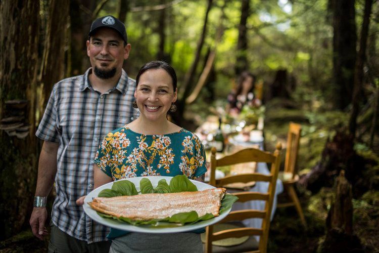 A man and a woman are holding a plate of food in the woods.