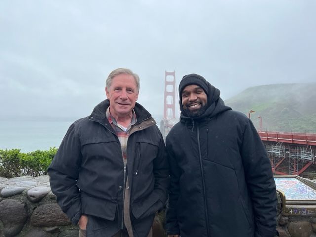 Two men are posing for a picture in front of the golden gate bridge.