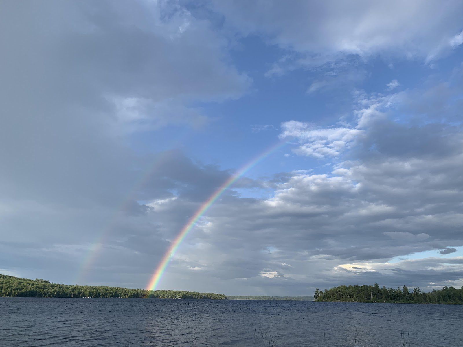 There is a rainbow in the sky over a lake.