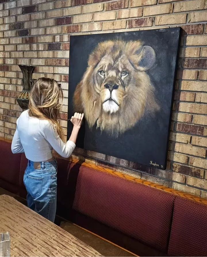 A woman is painting a picture of a lion on a brick wall.