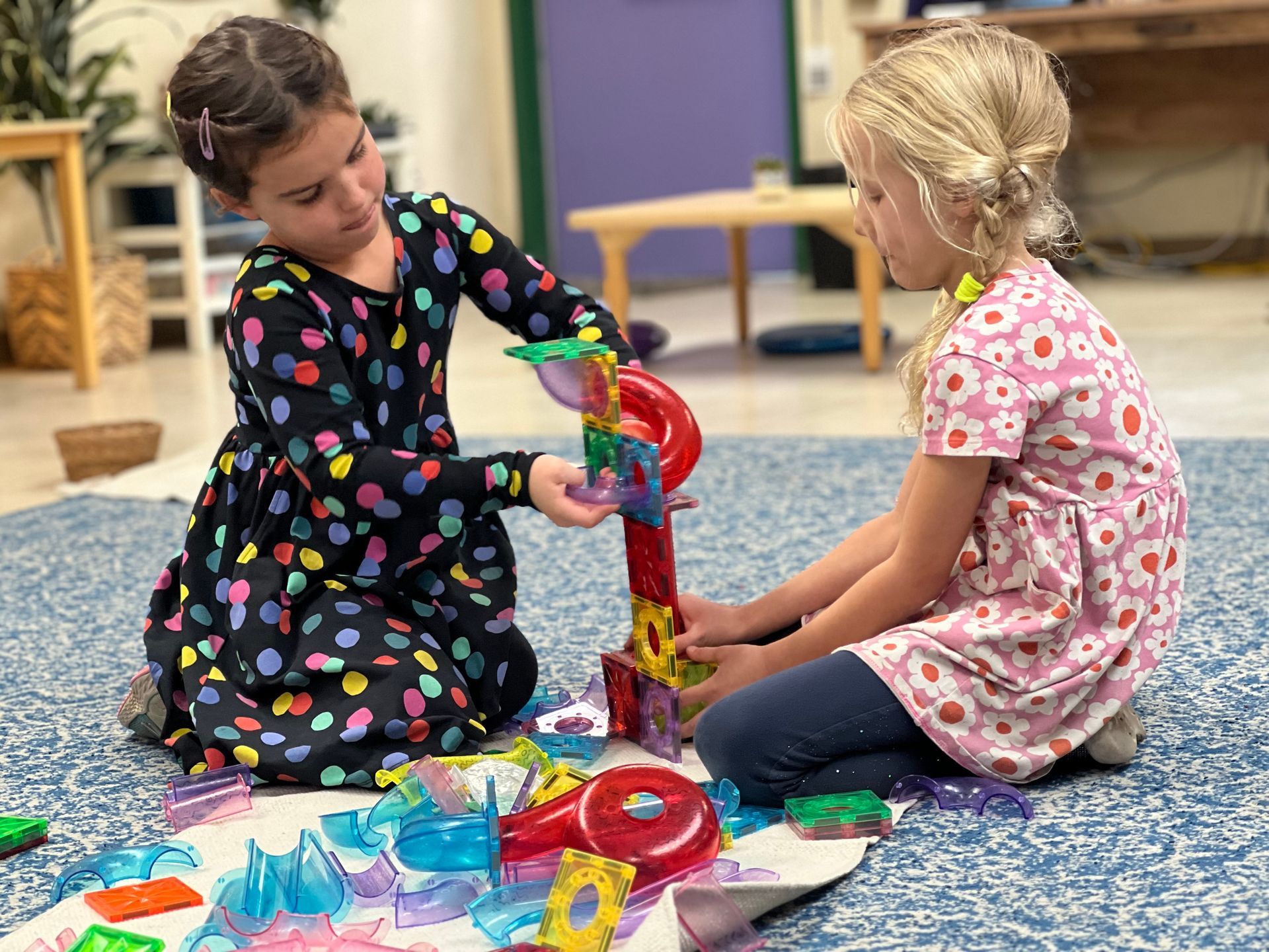 Montessori children are sitting on the floor working with magnetic tiles