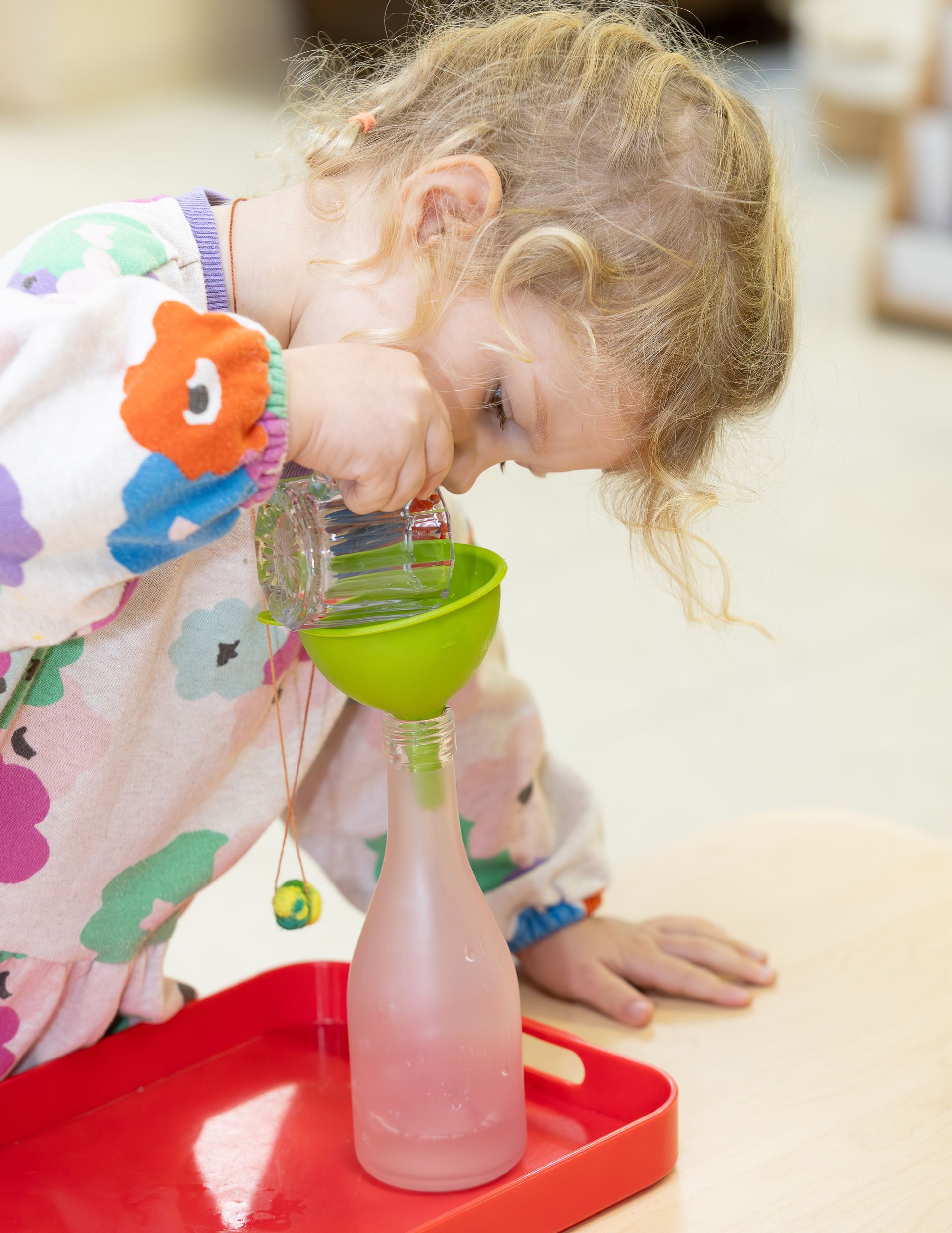 Montessori child pouring water into a bottle.