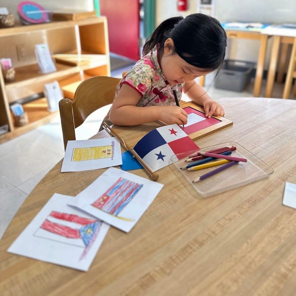 Montessori child is sitting at a table drawing a flag