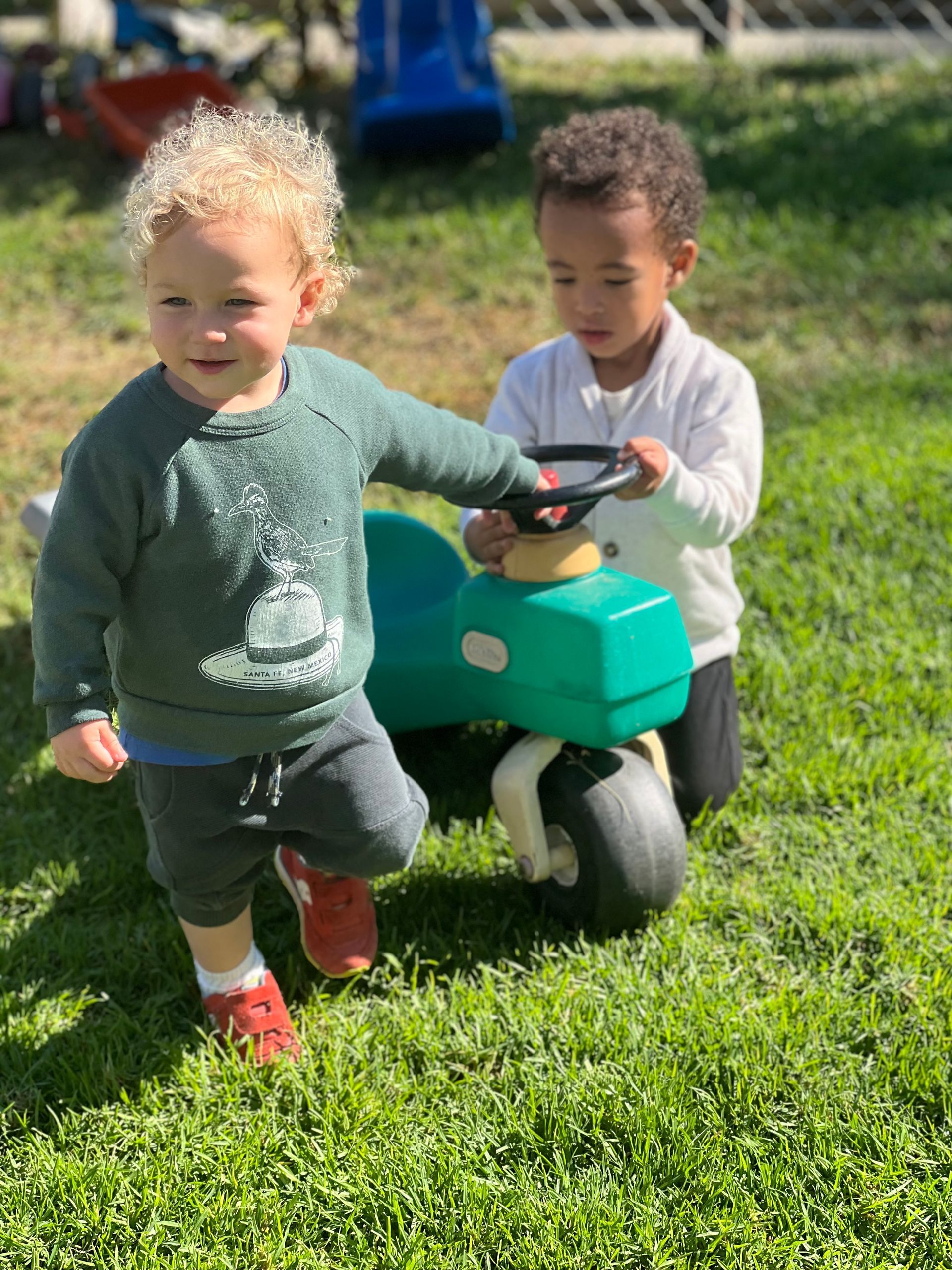 Montessori children are playing with a toy car in the grass.