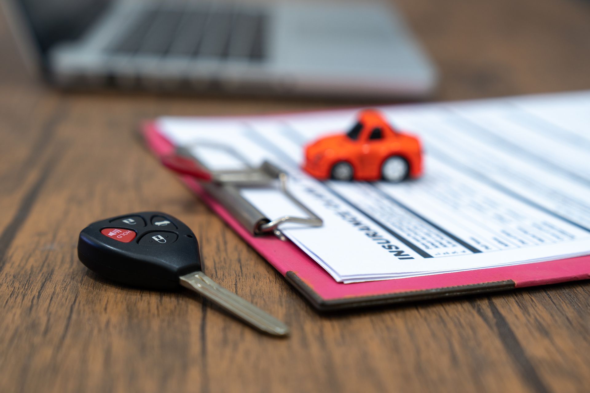 Chiavi dell'auto e macchinina giocattolo sulla documentazione assicurativa, vicino a un computer portatile.