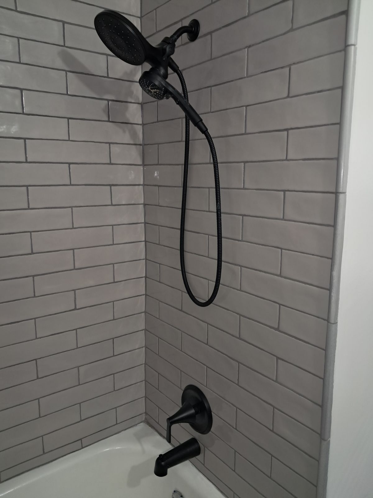 A shower head is hanging from a brick wall next to a bathtub.