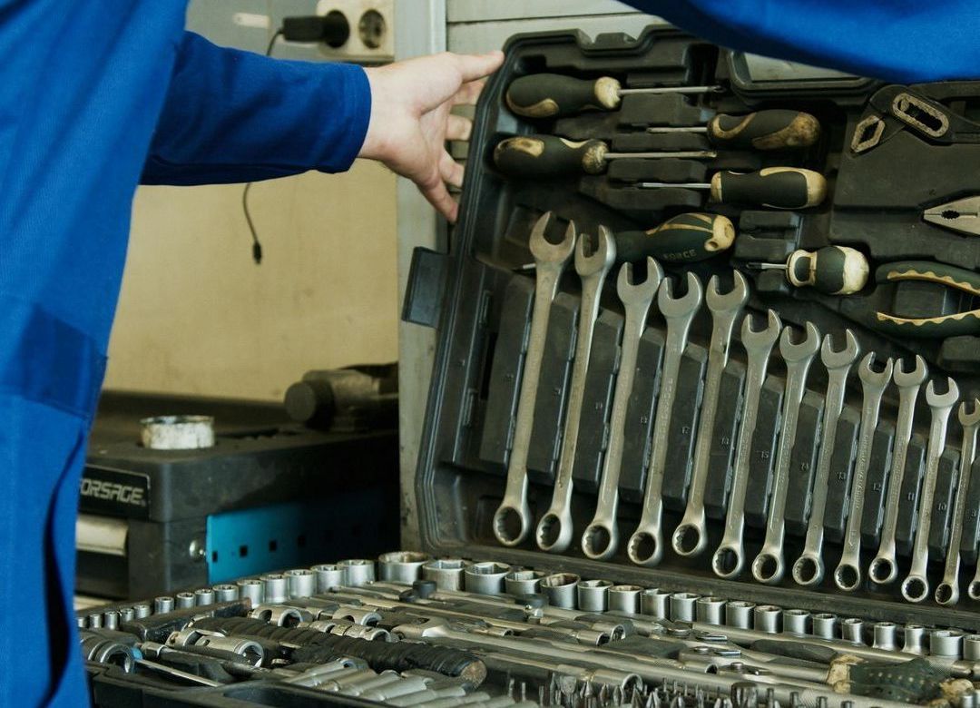 Homme en bleu de travail ouvre une grosse boite à outils contenant tournevis, pinces, boulons, clés etc