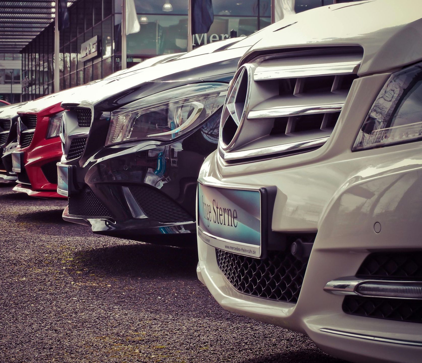 Devant de véhicules de luxe mercedes blanc, rouge, noir, gris, alignés sur un parking devant une concession
