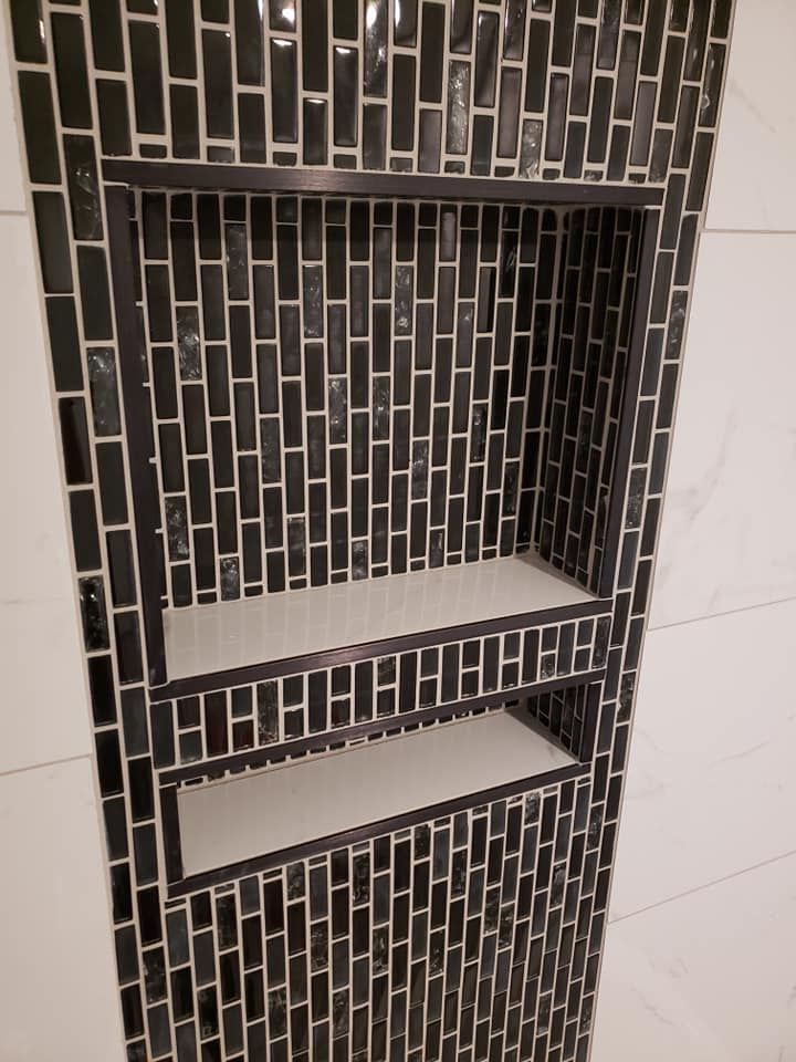 A shower niche with black tiles and white shelves.