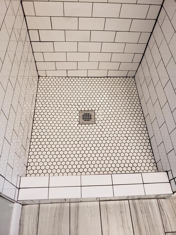 A shower stall with white tiles and a drain