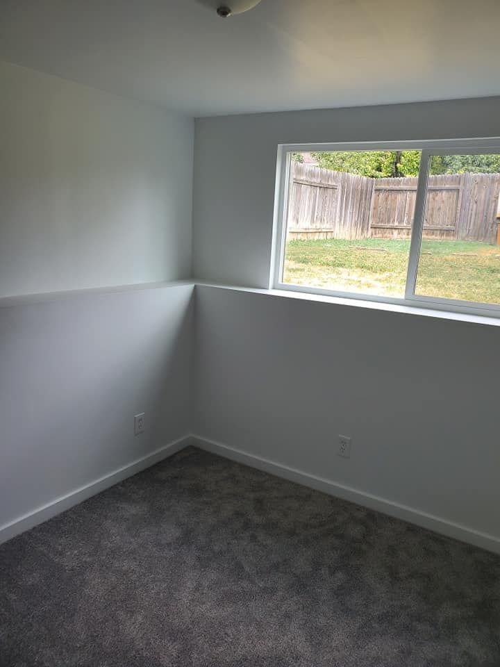 An empty bedroom with a large window and a fence in the background.