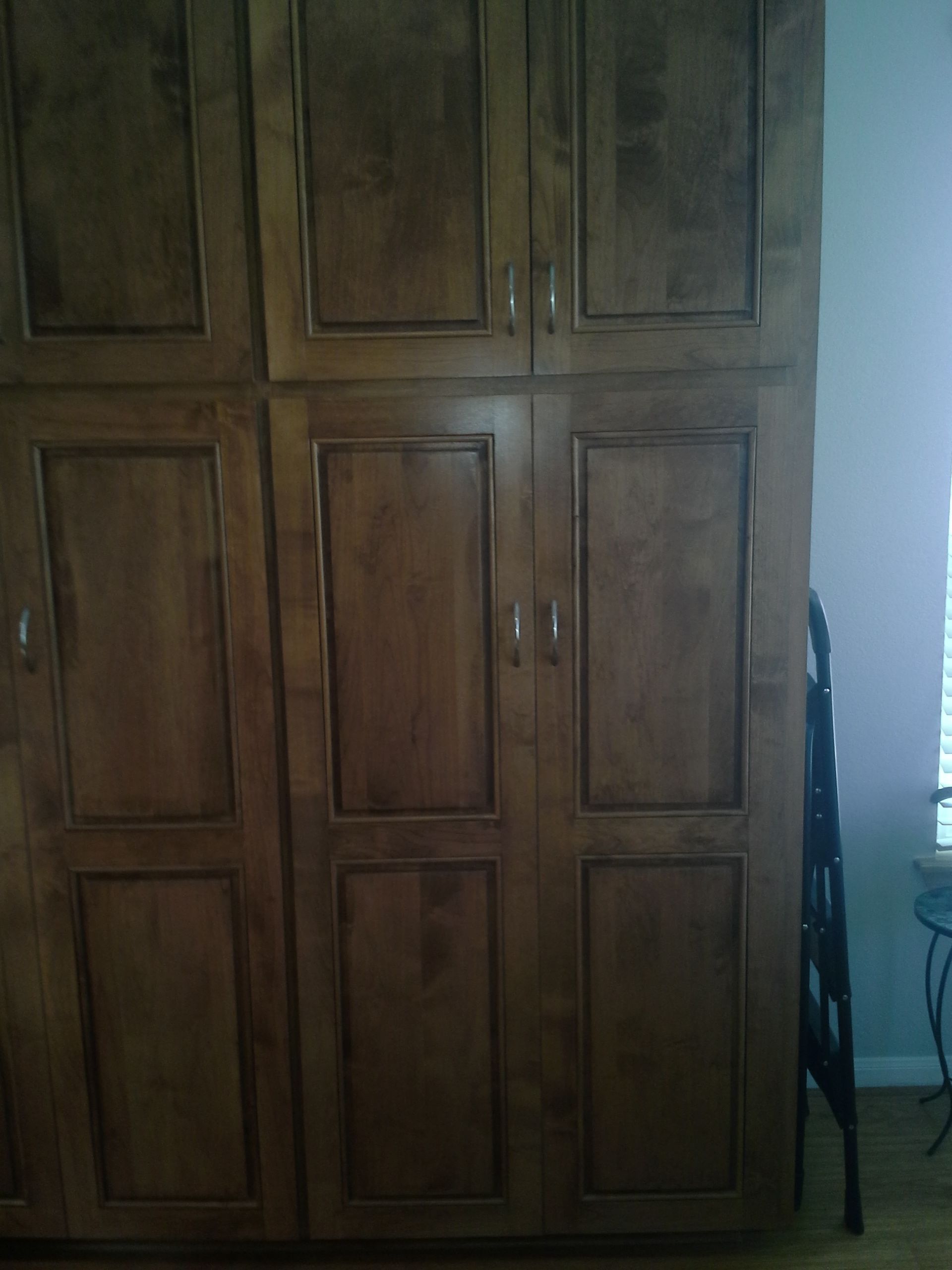 A large wooden cabinet is sitting in a room next to a chair.