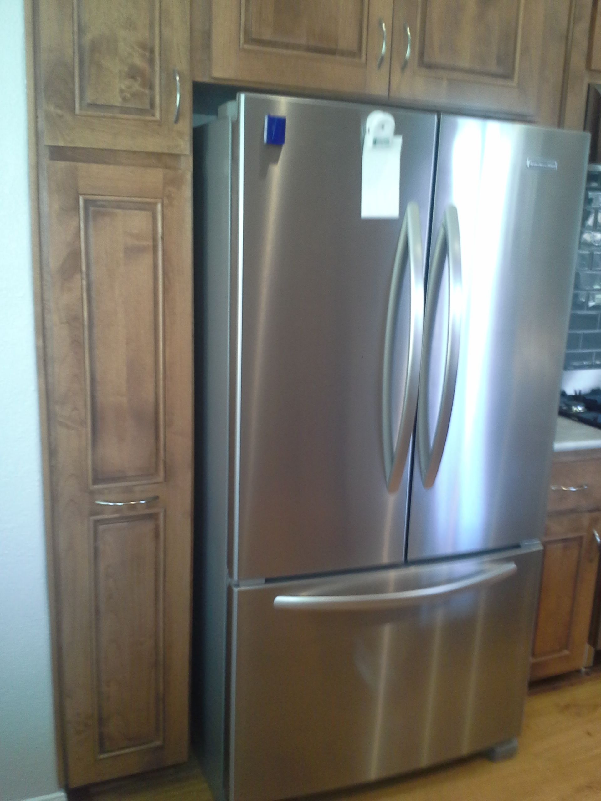A stainless steel refrigerator in a kitchen with wooden cabinets